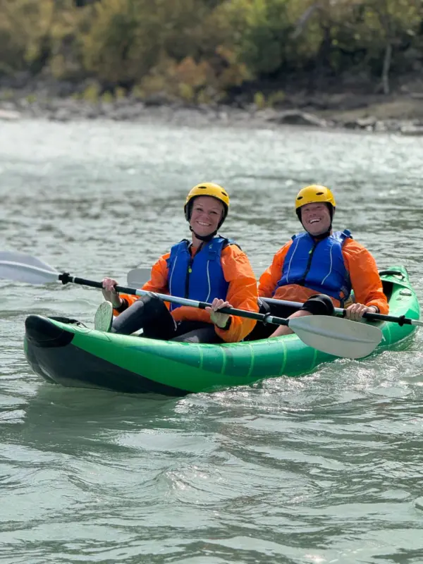 Two people in a green tandem kayak on the calm turquoise Vjosa River near Përmet