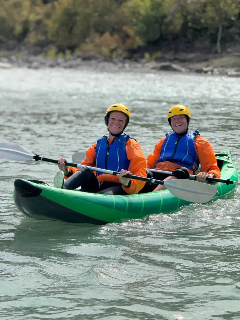 Two people in a green tandem kayak on the calm turquoise Vjosa River near Përmet