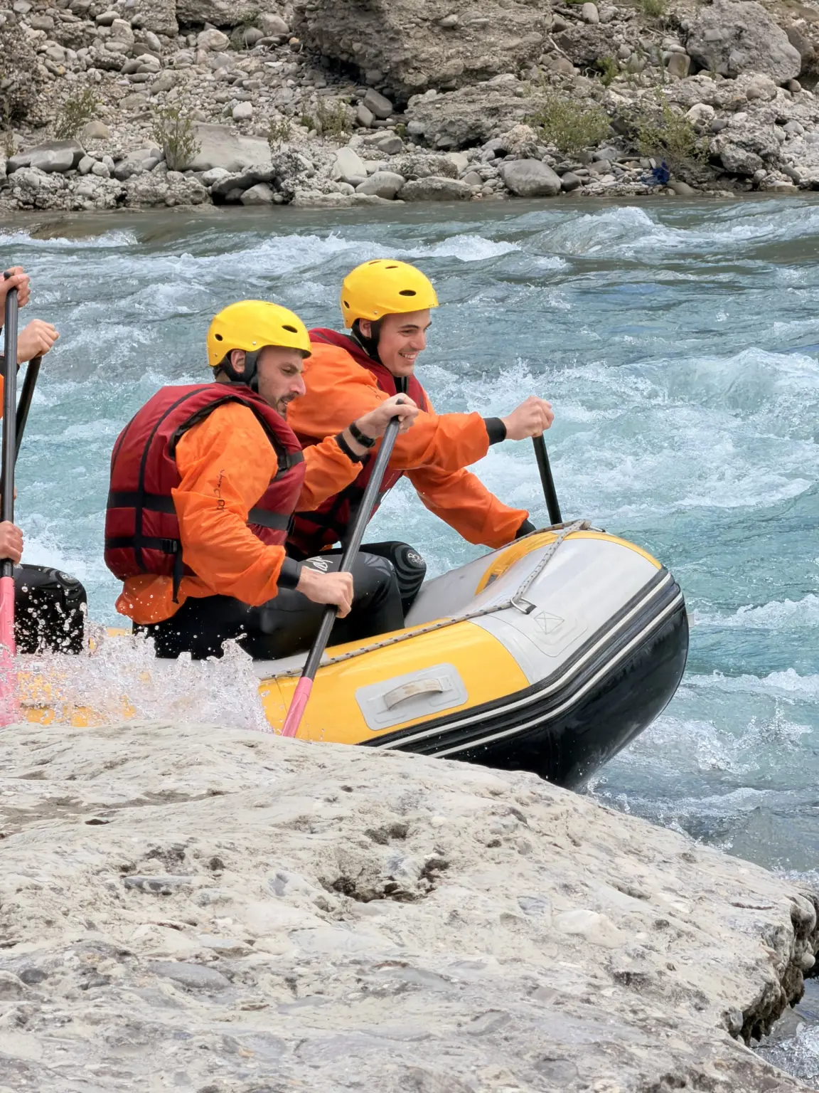 Guide and guest in orange life jackets on a raft at the edge of a Vjosa rapid