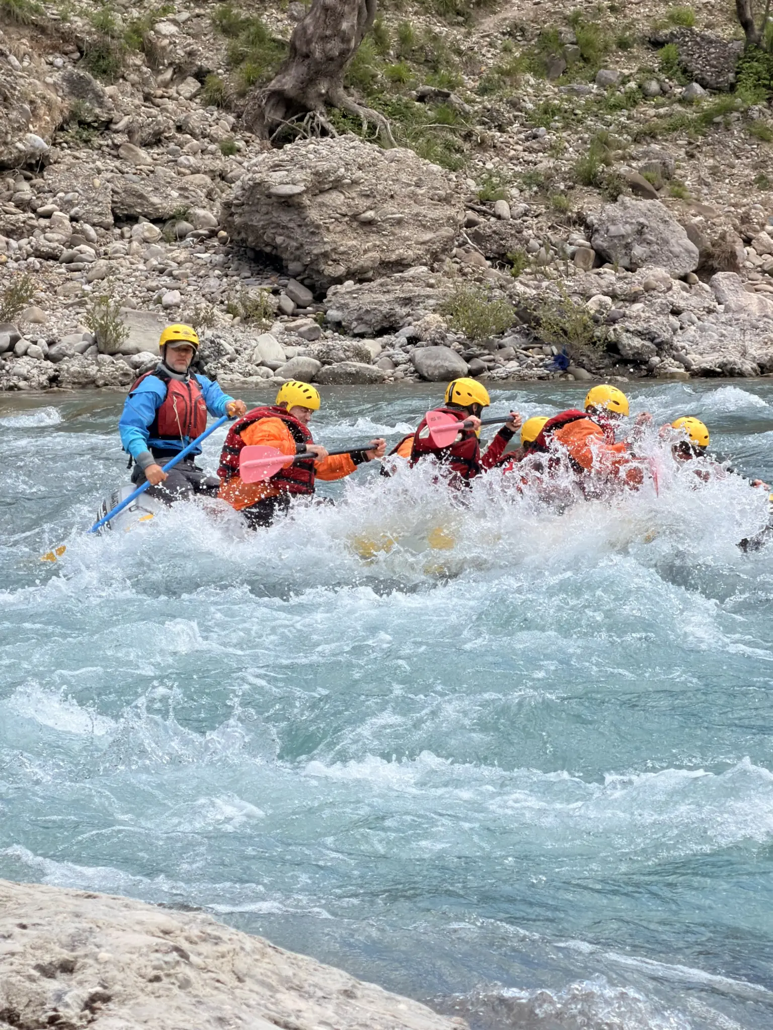 Guide steering a raft through a rapid beside a limestone wall on the Vjosa