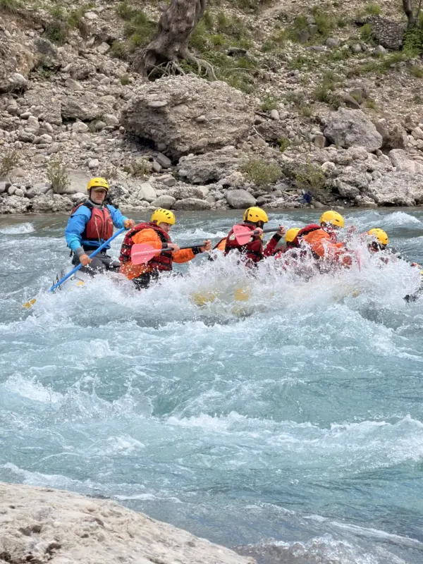 Guide steering a raft through a rapid beside a limestone wall on the Vjosa