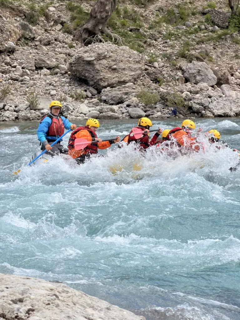 Guide steering a raft through a rapid beside a limestone wall on the Vjosa
